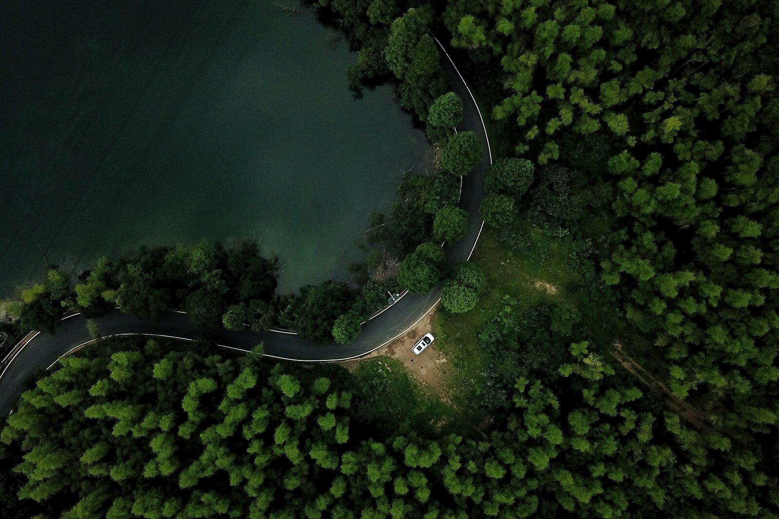 Letecký pohled na klikatou silnici podél tmavě zeleného jezera v hustém lese.