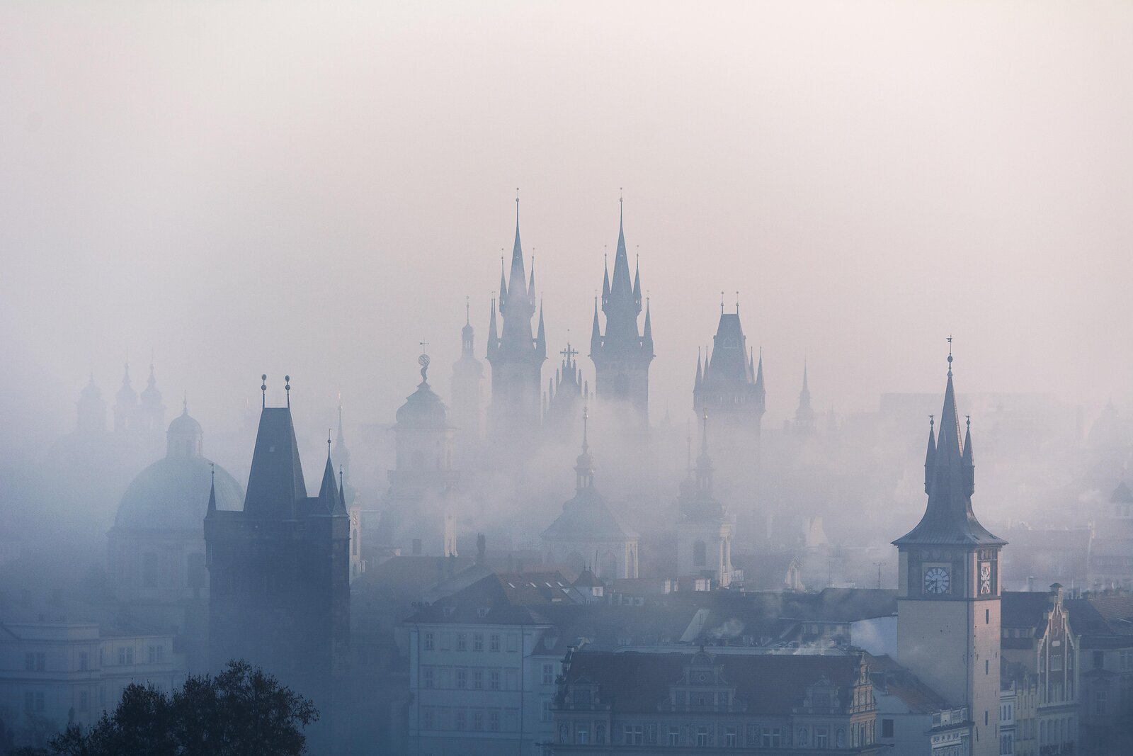 Siluety pražských historických věží a střech v ranní mlze