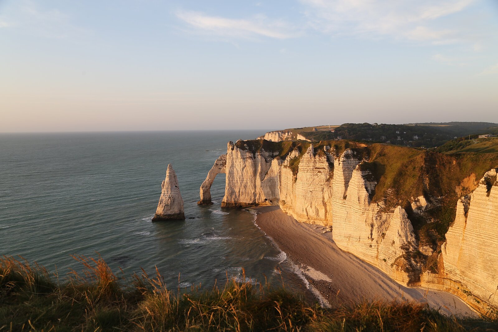 Křídové útesy Étretat se skalním obloukem a mořským jehlanem v teplém večerním světle